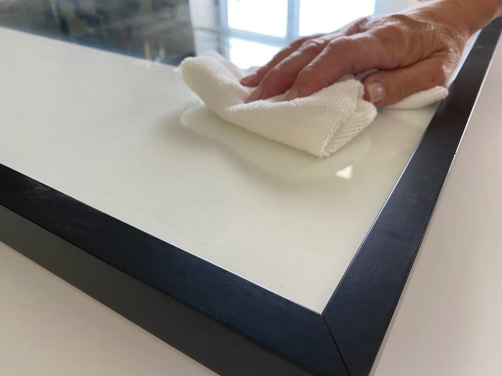 hand with a white towel wiping the surface of a glass frame